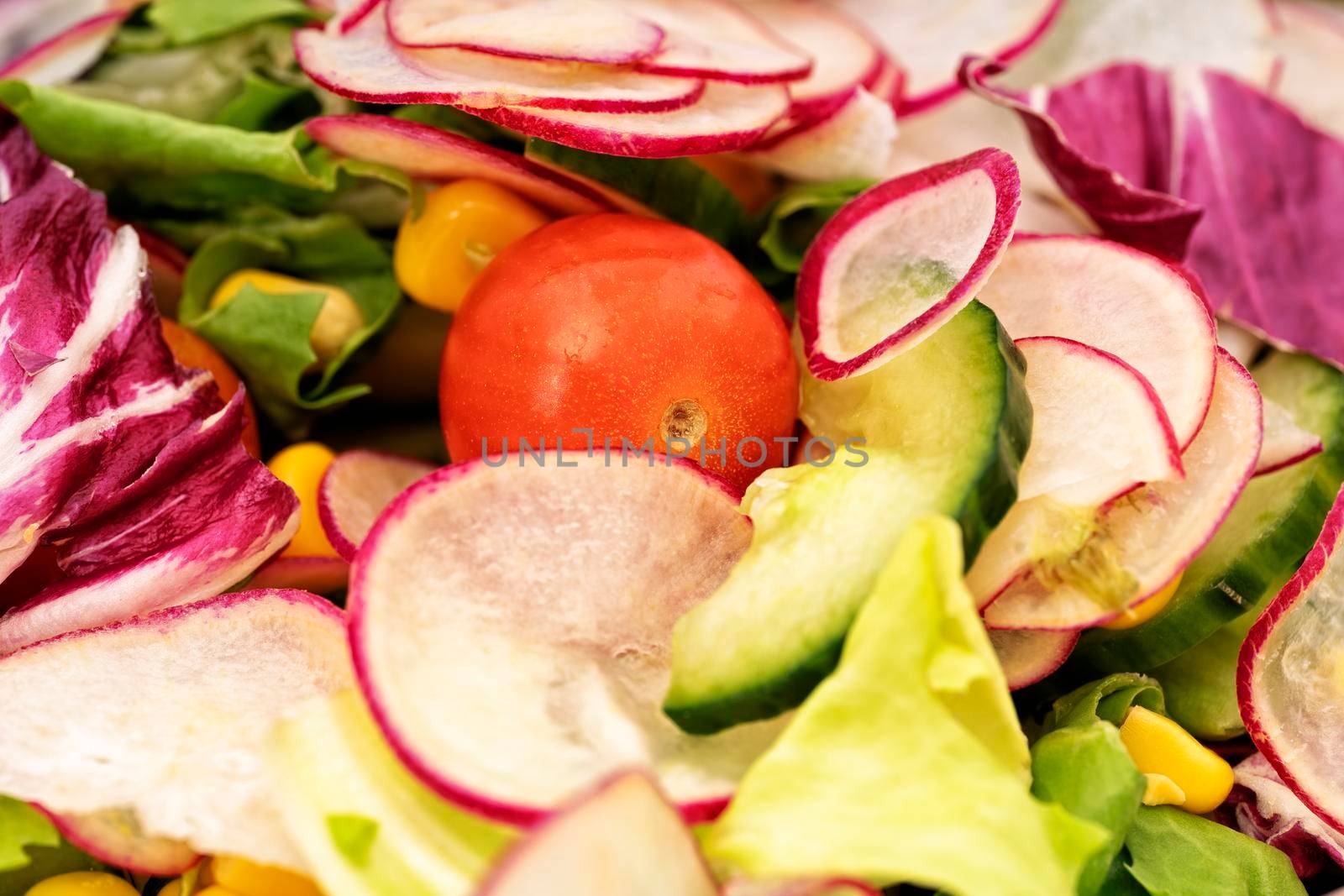 Close up of fresh healthy salad with cherry tomatoes, cucumber, radishes, and mixed greens. Healthy food concept.