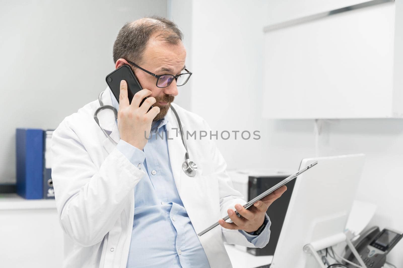Doctor in office talking on phone by HERRAEZ