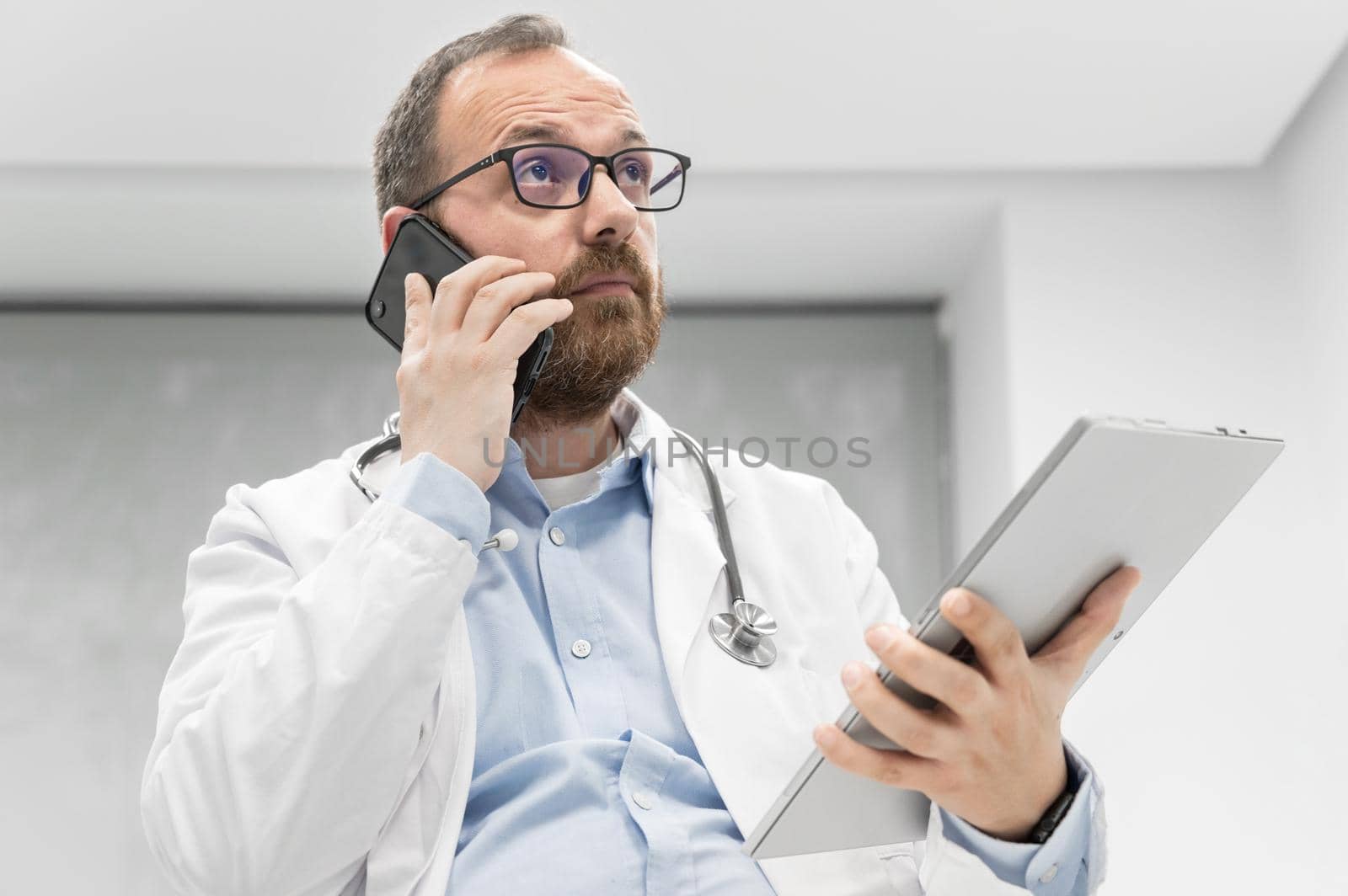 Doctor in office talking on phone by HERRAEZ