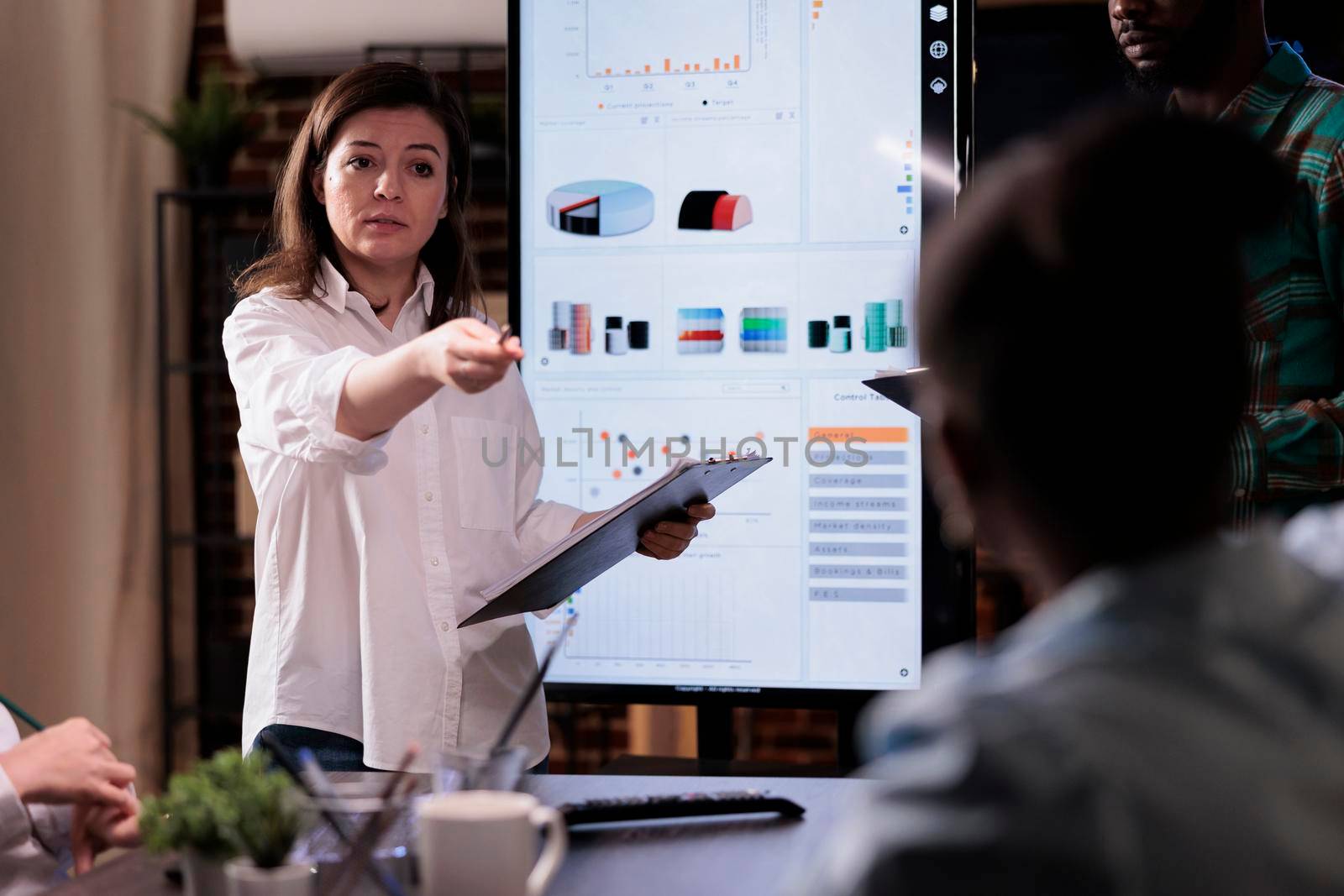 Caucasian business woman holding clipboard pointing at coworker asking question about sales performance by DCStudio