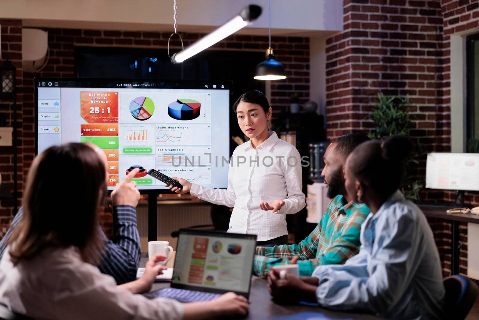 Employee standing in front of team of coworkers presenting sales strategy using remote control by DCStudio