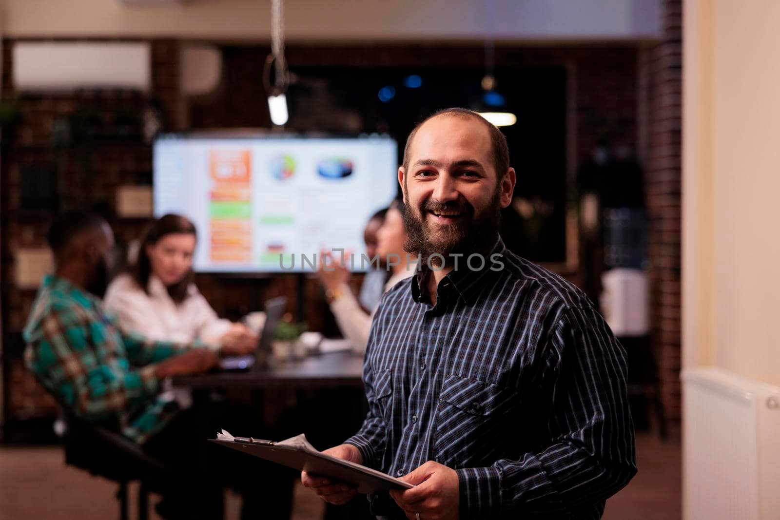 Portrait of smiling caucasian business employee holding laptop in startup office working overtime by DCStudio