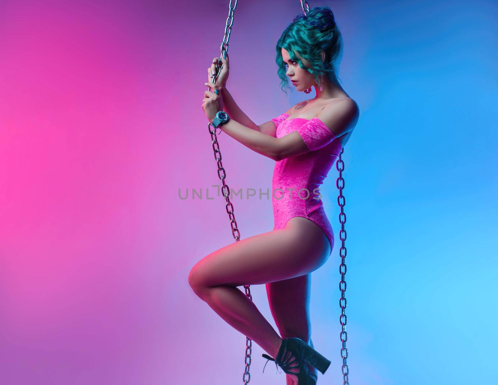 the sexy girl with colored hair in a bright pink bodysuit with a metal chain on a neon background