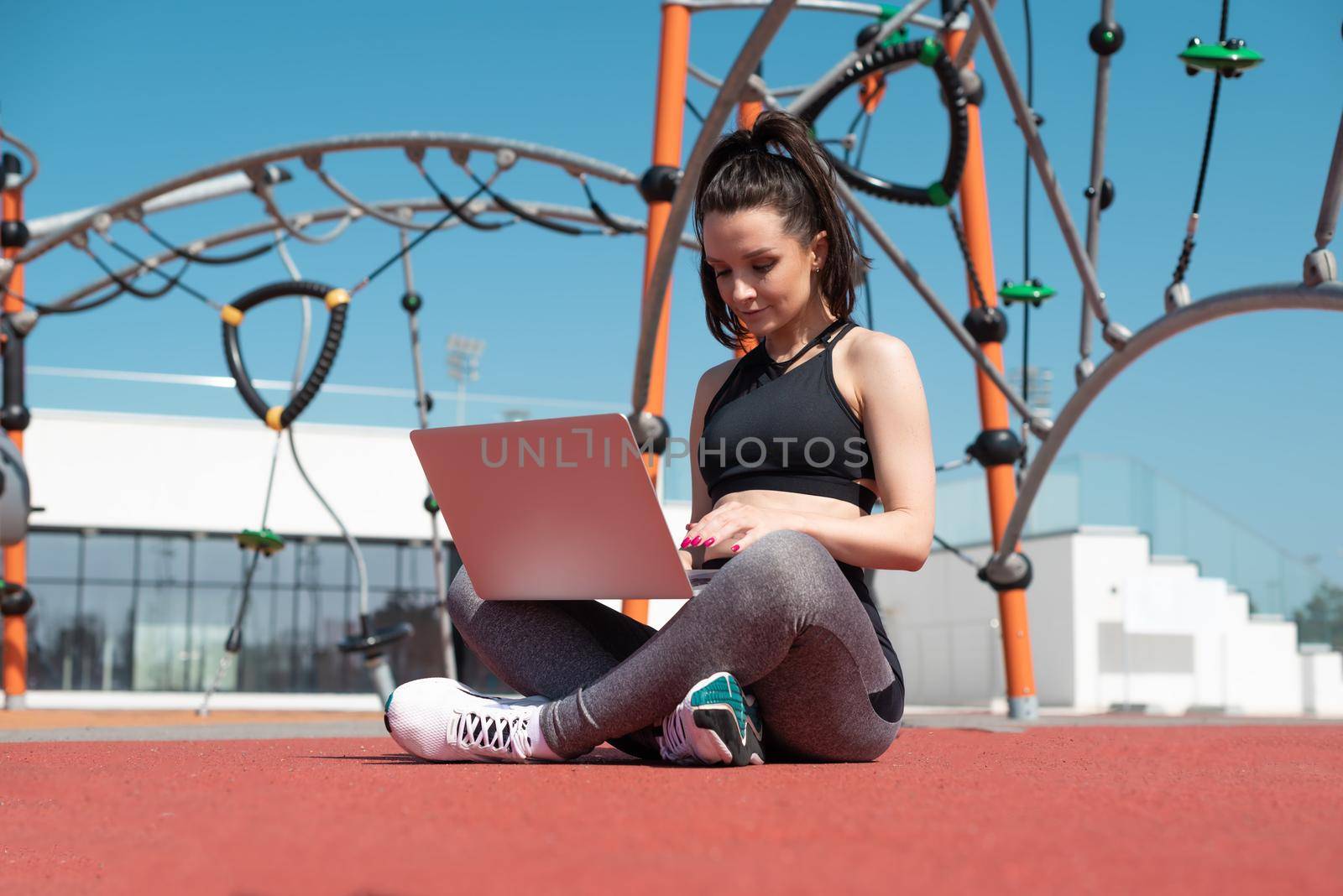 girl in sportswear on a summer outdoor sports field is sitting with a laptop