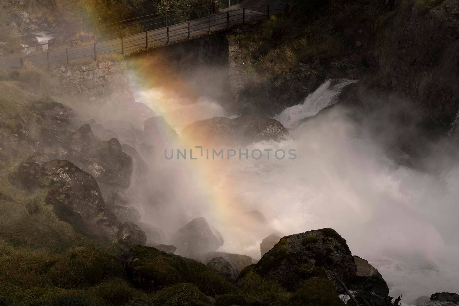 Waterfall crossing under a bridge and the rainbow in a rocky mountain on the way to Briksdal glacier in Norway