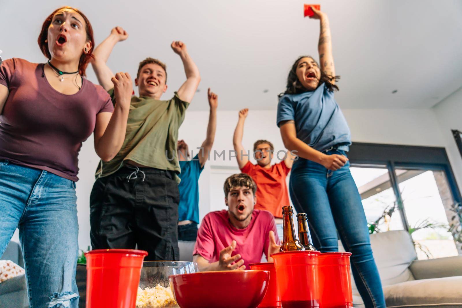 friends jumping for joy watching e-sports on TV after their team's victory. group of young watching soccer on tv. by CatPhotography