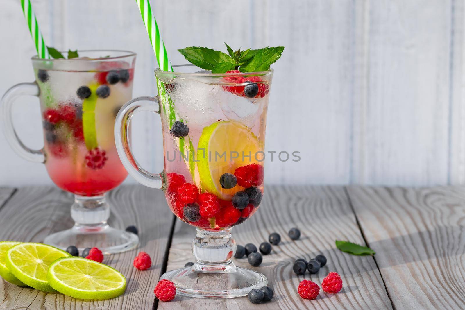 Fresh homemade summer cocktails with ice, lime and berries in glasses with a straw, copyspace.