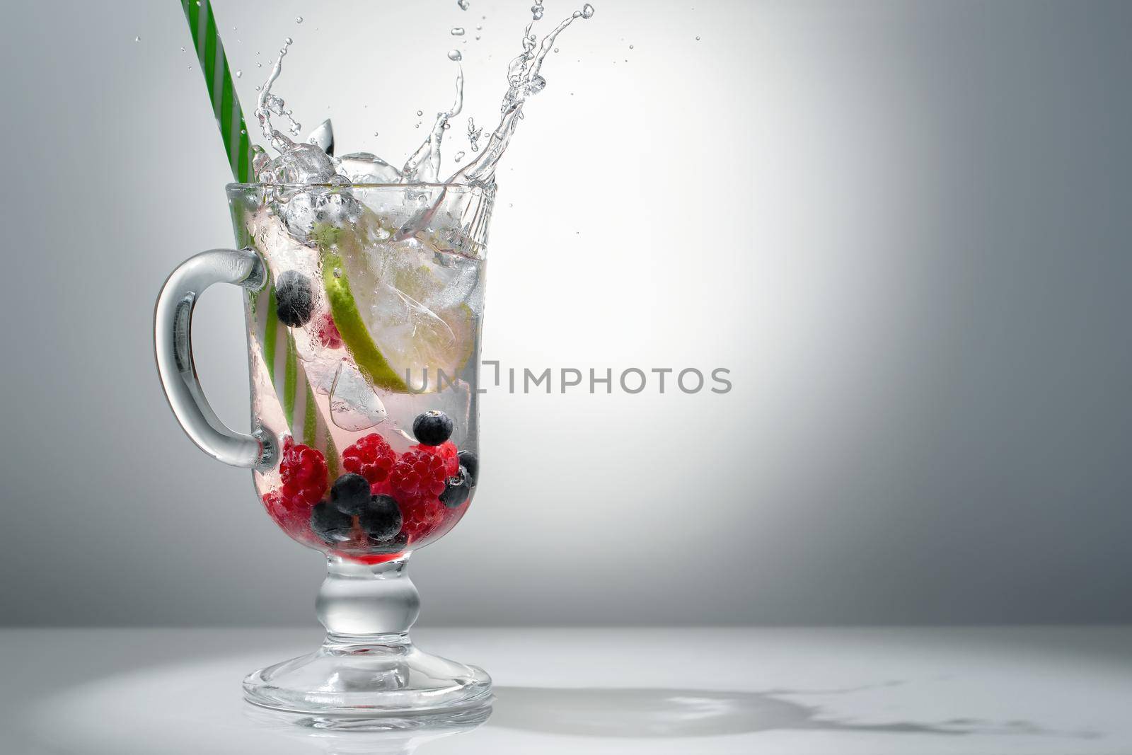 Refreshing summer cocktail with ice, lime and berries in a glass with a straw, copyspace.