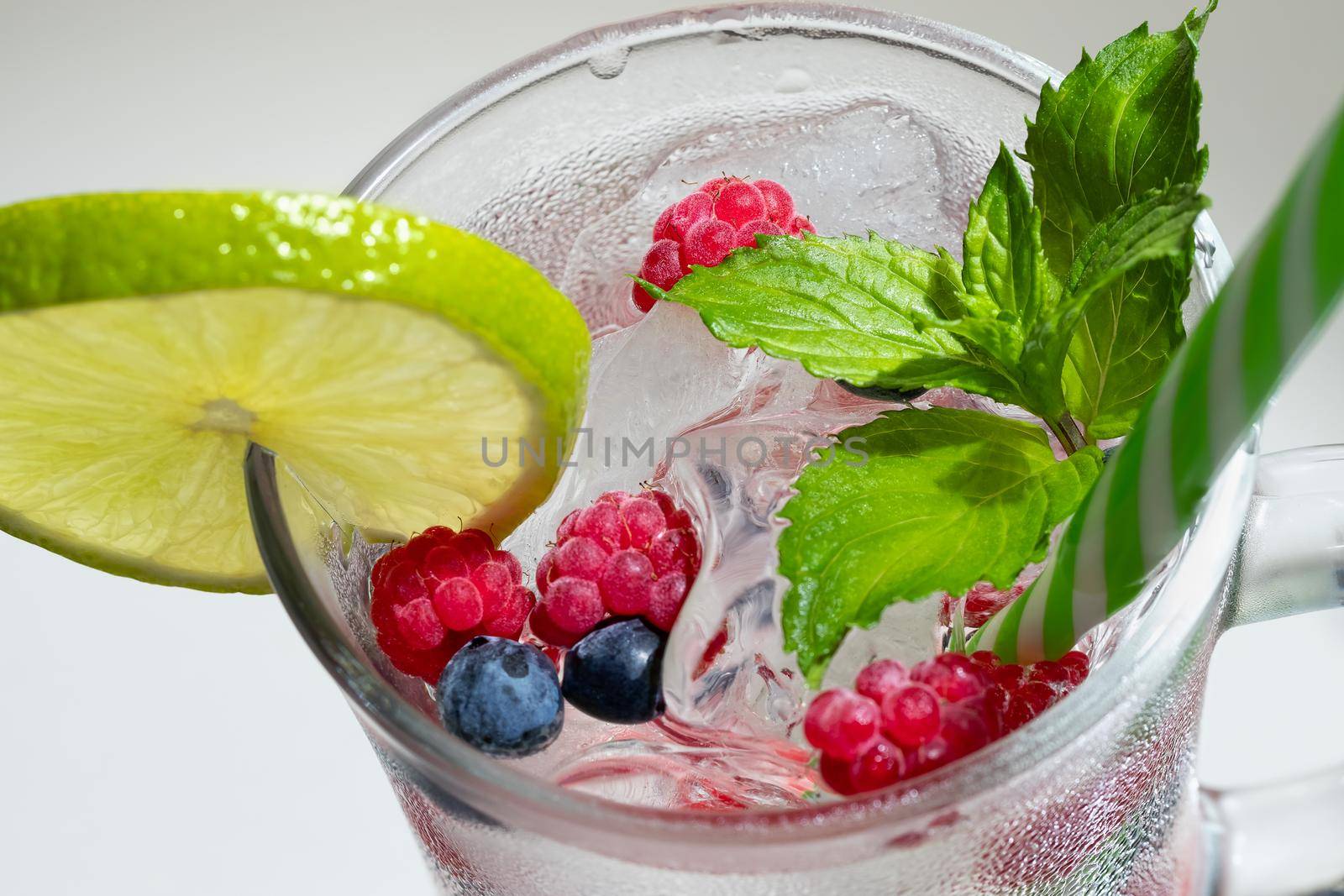 Refreshing summer cocktail with ice, lime and berries in a glass with a straw by galsand