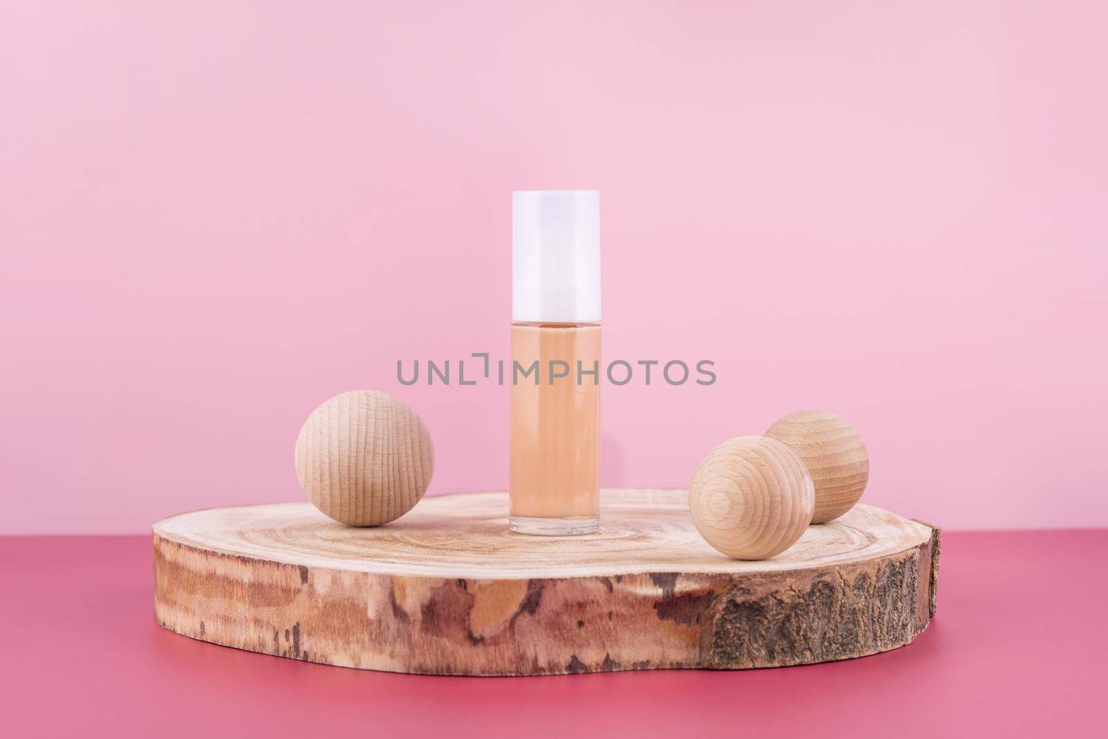 Cosmetic liquid foundation nude cream bottle mockup on wooden podium and decor balls. Beige concealer base cosmetics product mock up on pink background. Skincare beauty primer, bb corrector