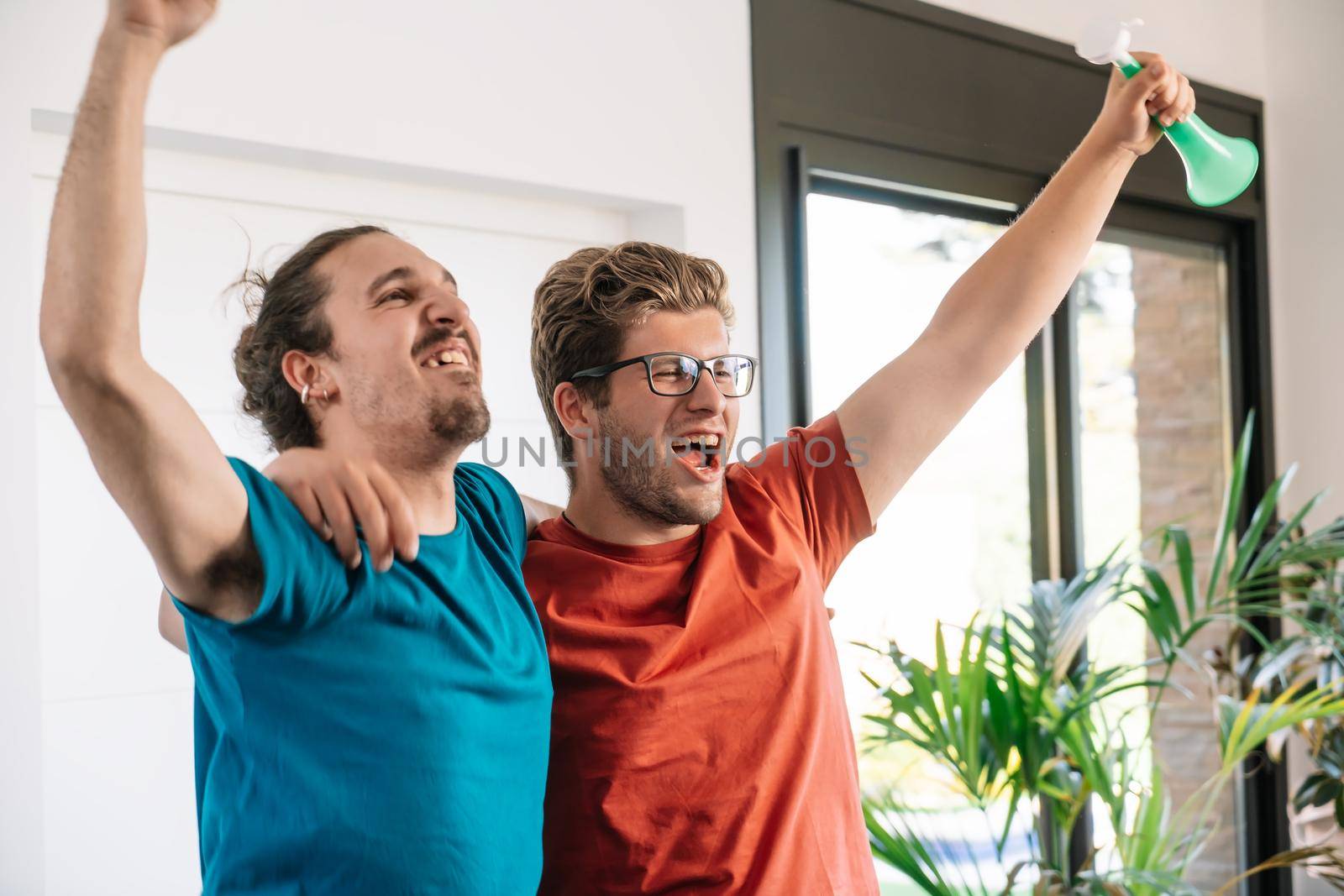 friends hugging after the victory of their sports team broadcast on television. group of young people partying at home. concept leisure concept. happy and cheerful. natural light in the living room at home. trumpet