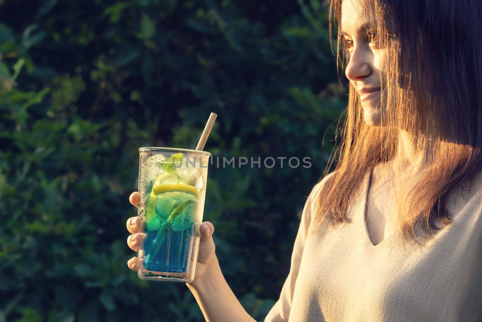 Young woman with long dark hair holds a summer refreshing cocktail in her hand. Selective focus.