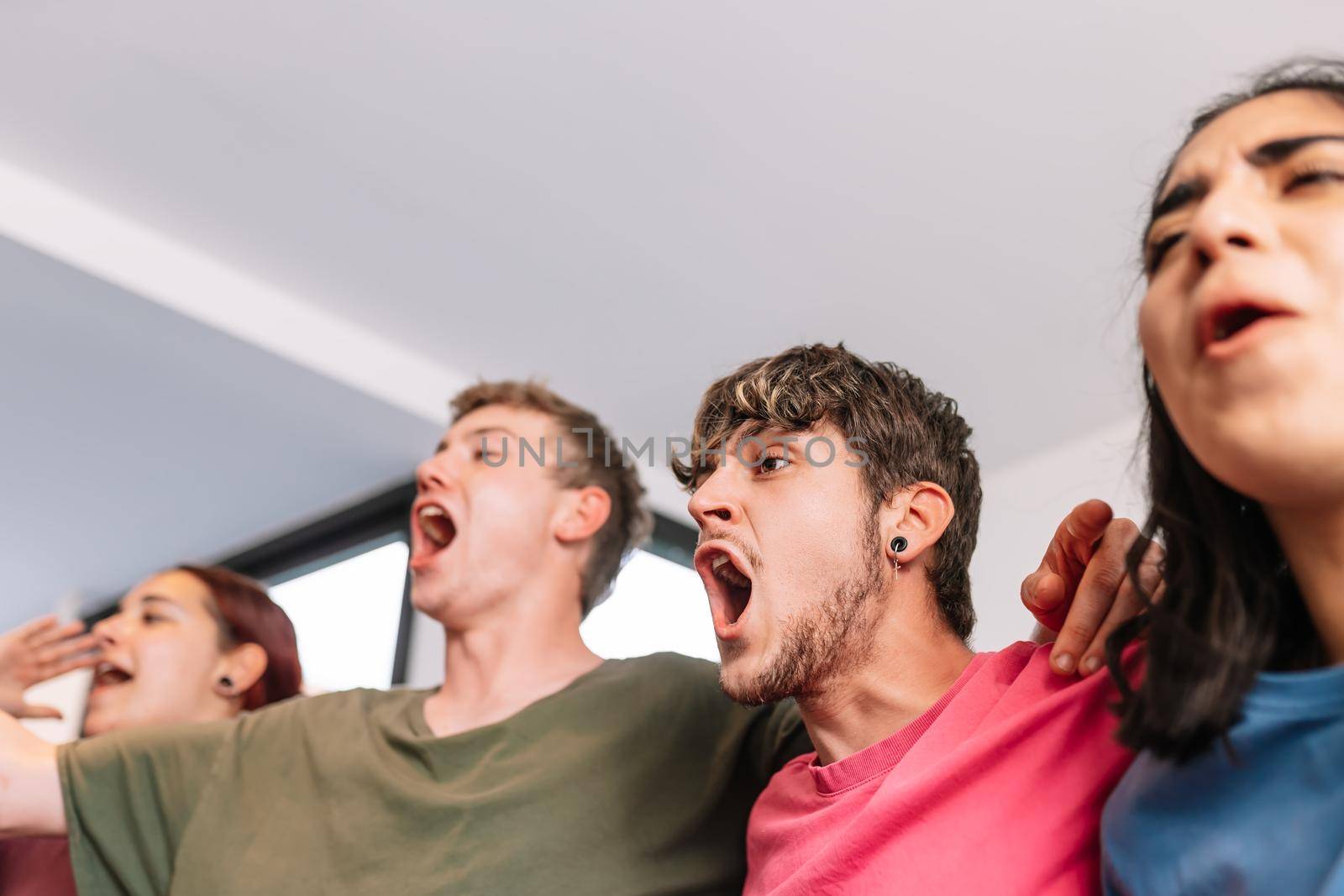 friends screaming with joy watching e-sports on TV after their team's victory. group of young people partying at home. leisure concept. happy and cheerful. natural light in the living room at home. trumpet