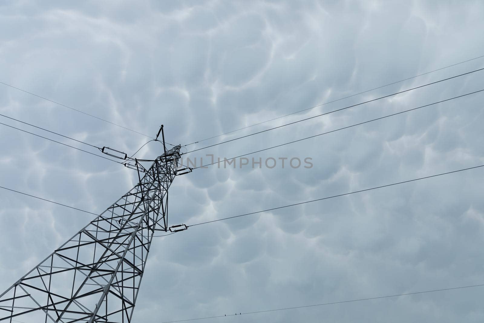 A tall power pole seen from below against a background of storm clouds in the shape of bubbles compressed one next to the other.