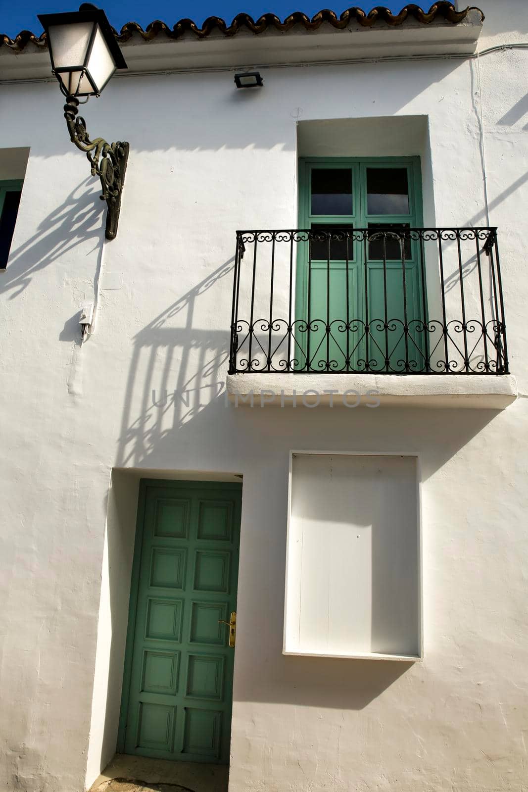 Whitewashed facade with vintage streetlight.Green wooden door and window in Altea, Alicante, Spain.