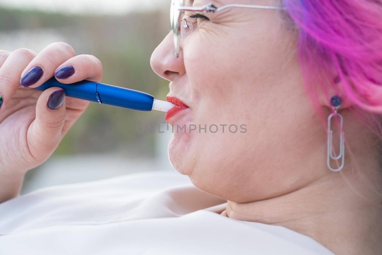 Caucasian woman with colored hair smokes an electronic cigarette