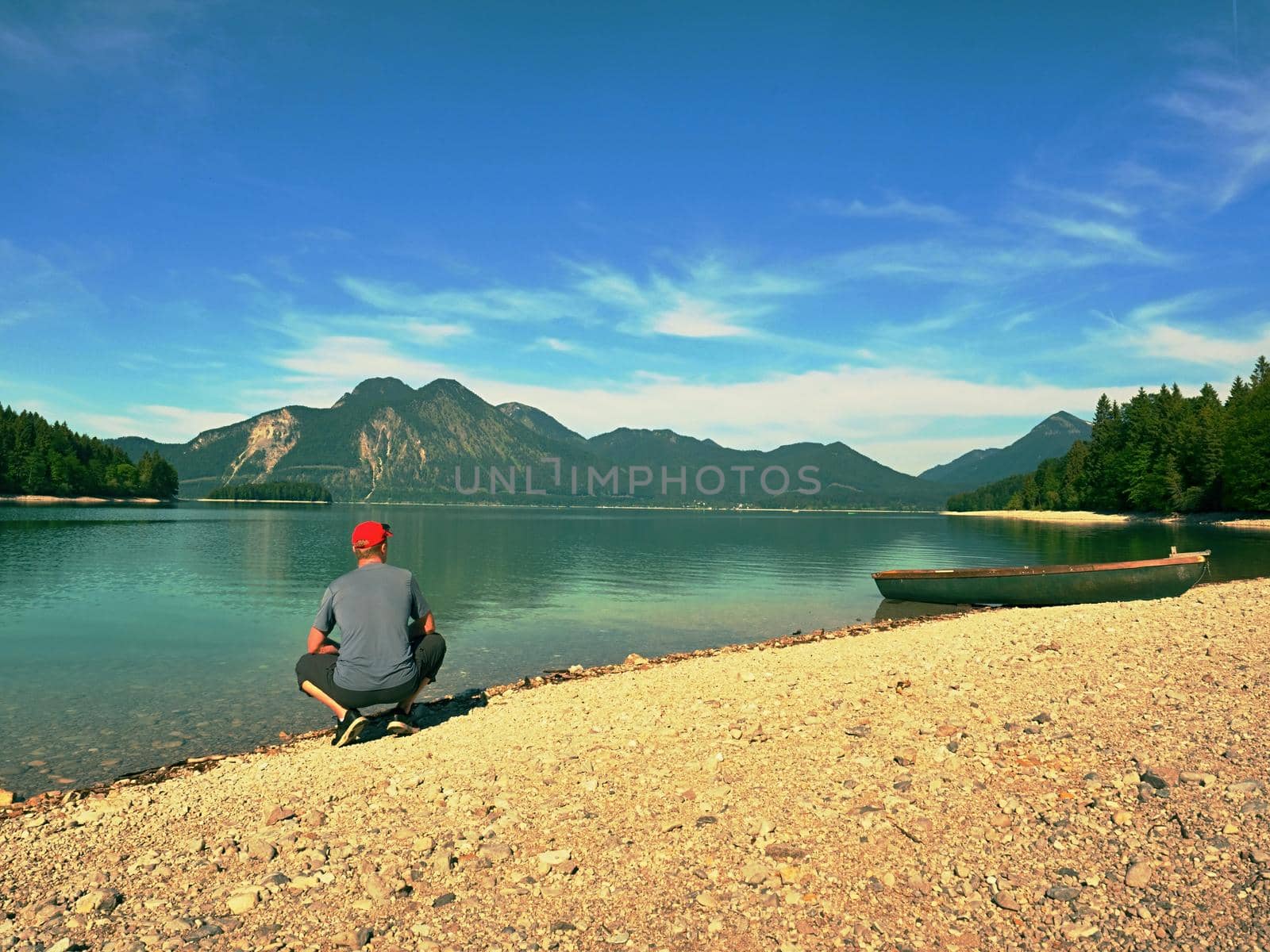 Man sitting on alpine mountain lake bank at anchored boat.  by rdonar2