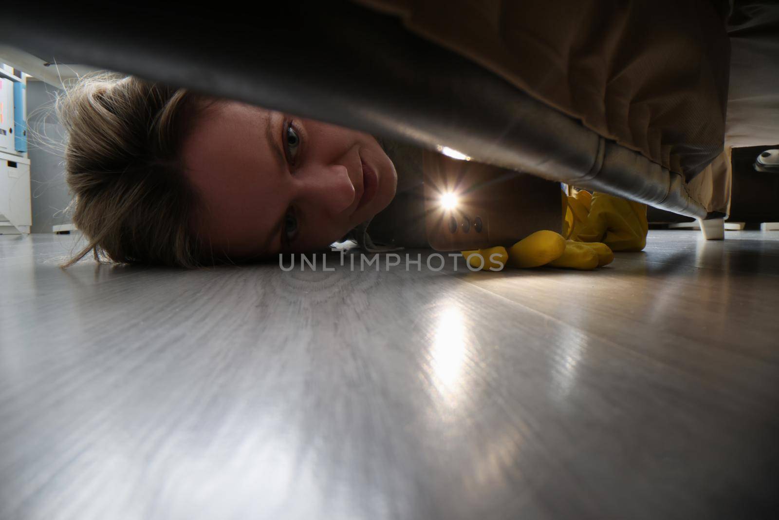 Woman using flashlight to look for something under bed by kuprevich