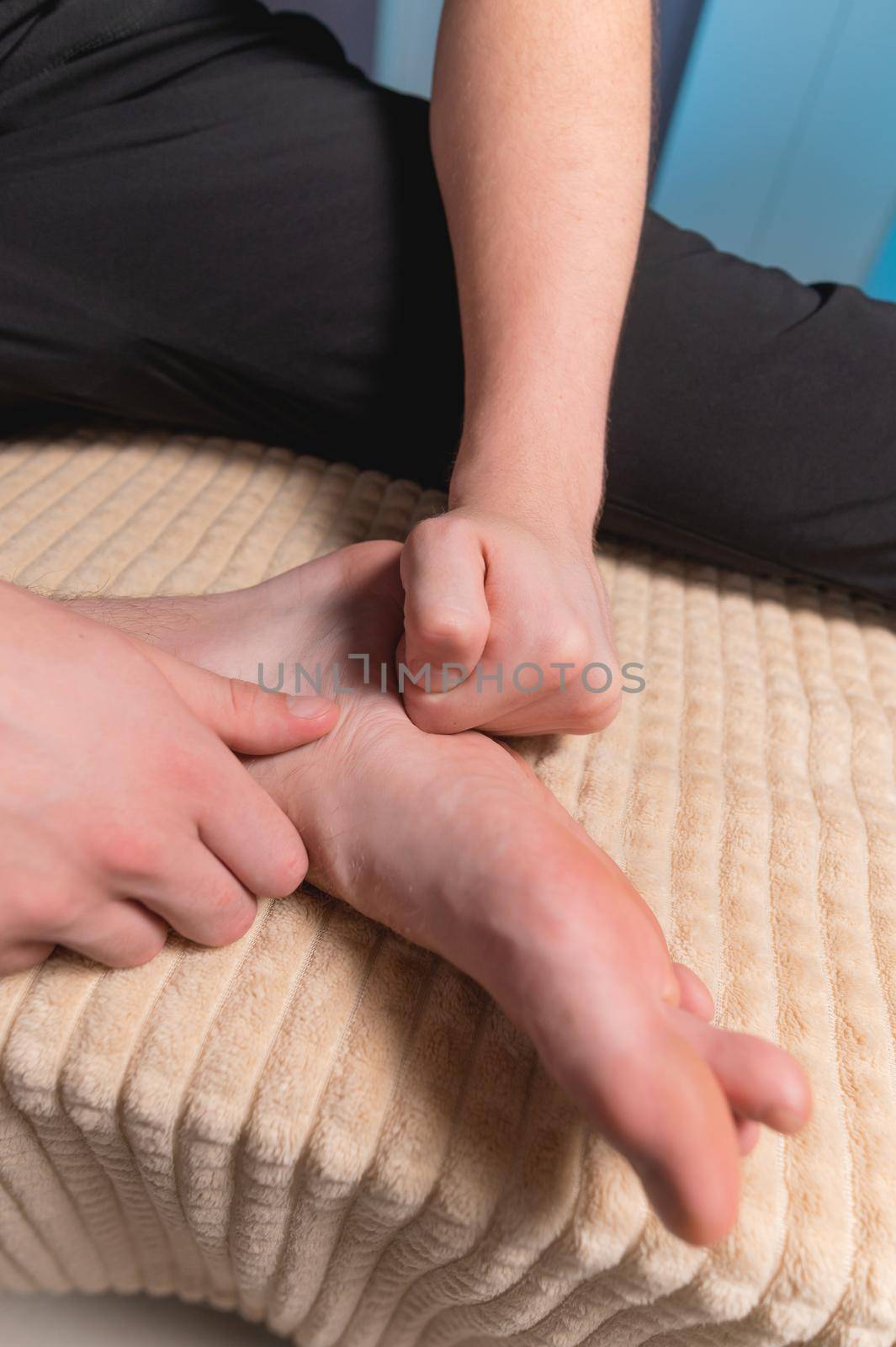 A man sitting on a massage table does self-massage of his feet with his own hands.