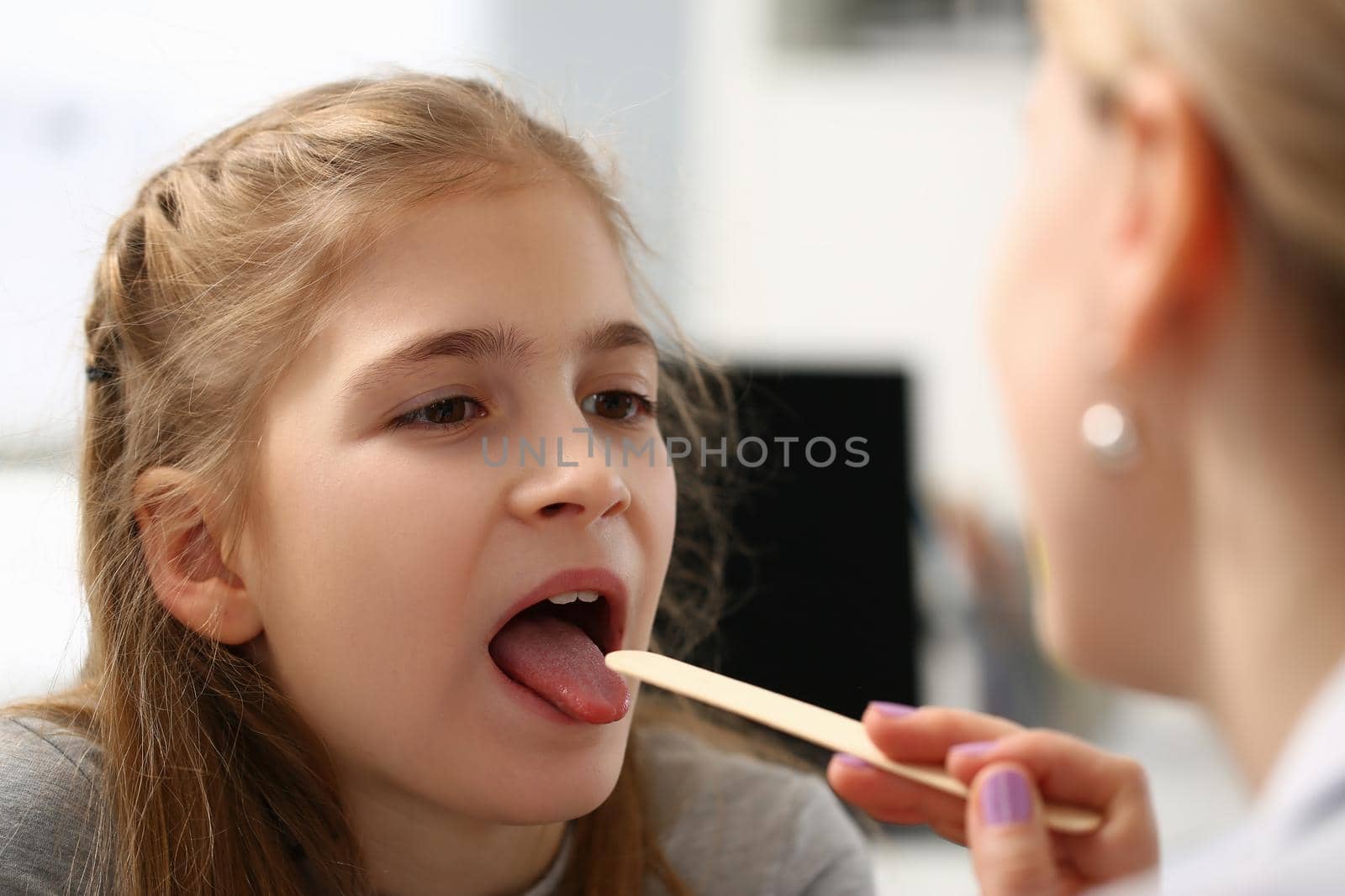 Portrait of pediatrician checking girls hurting throat with stick. Child open mouth for check up. Female doctor use tool for examination health. Medicine concept