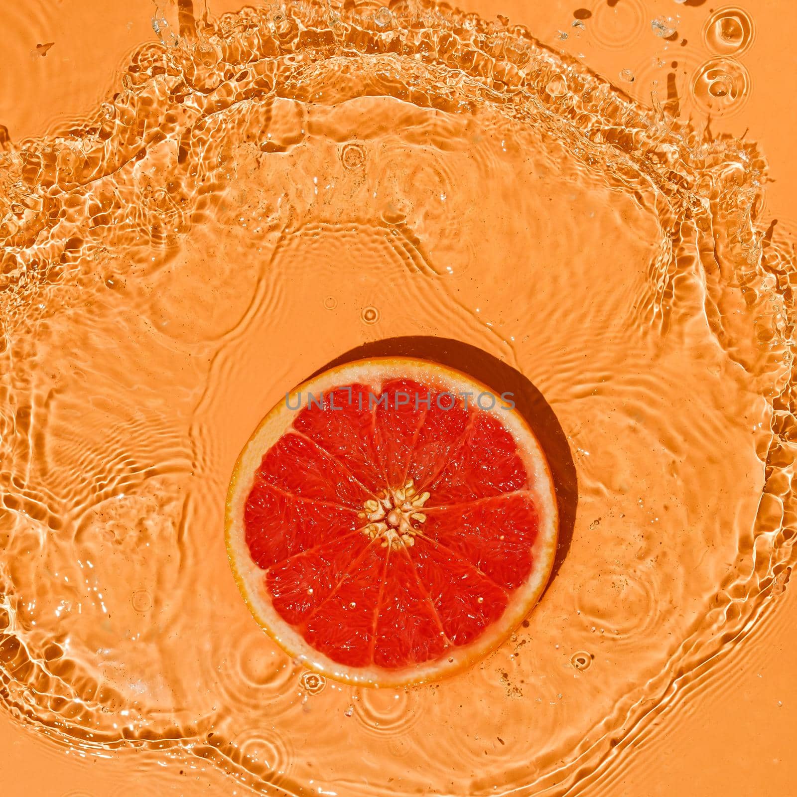Summer fruit concept citrus red grapefruit on a bright orange background with splashes of water movement.