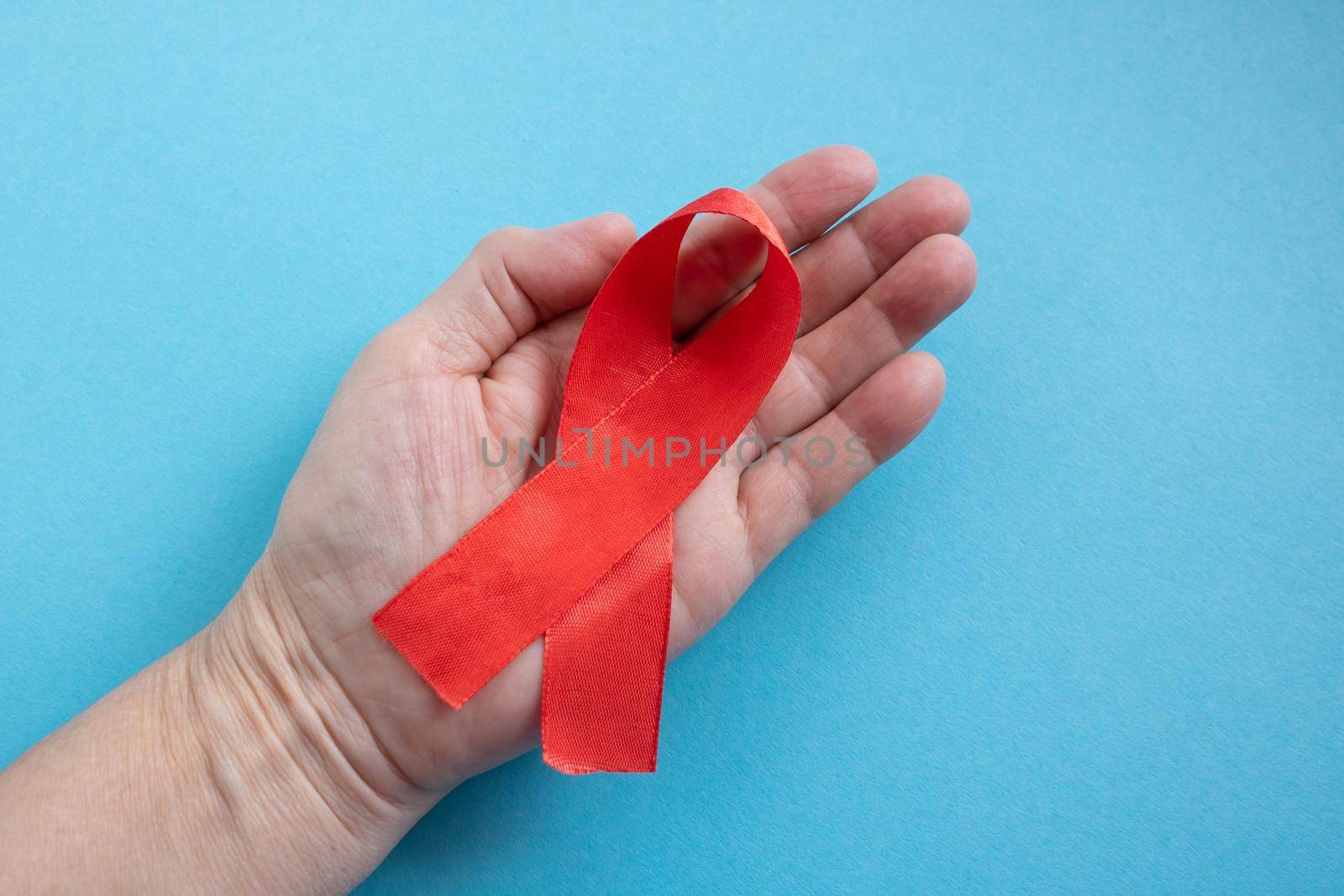 A hand holds a red ribbon on a blue background - the concept of World AIDS Day, Donor Day, Hemophilia Day by lapushka62