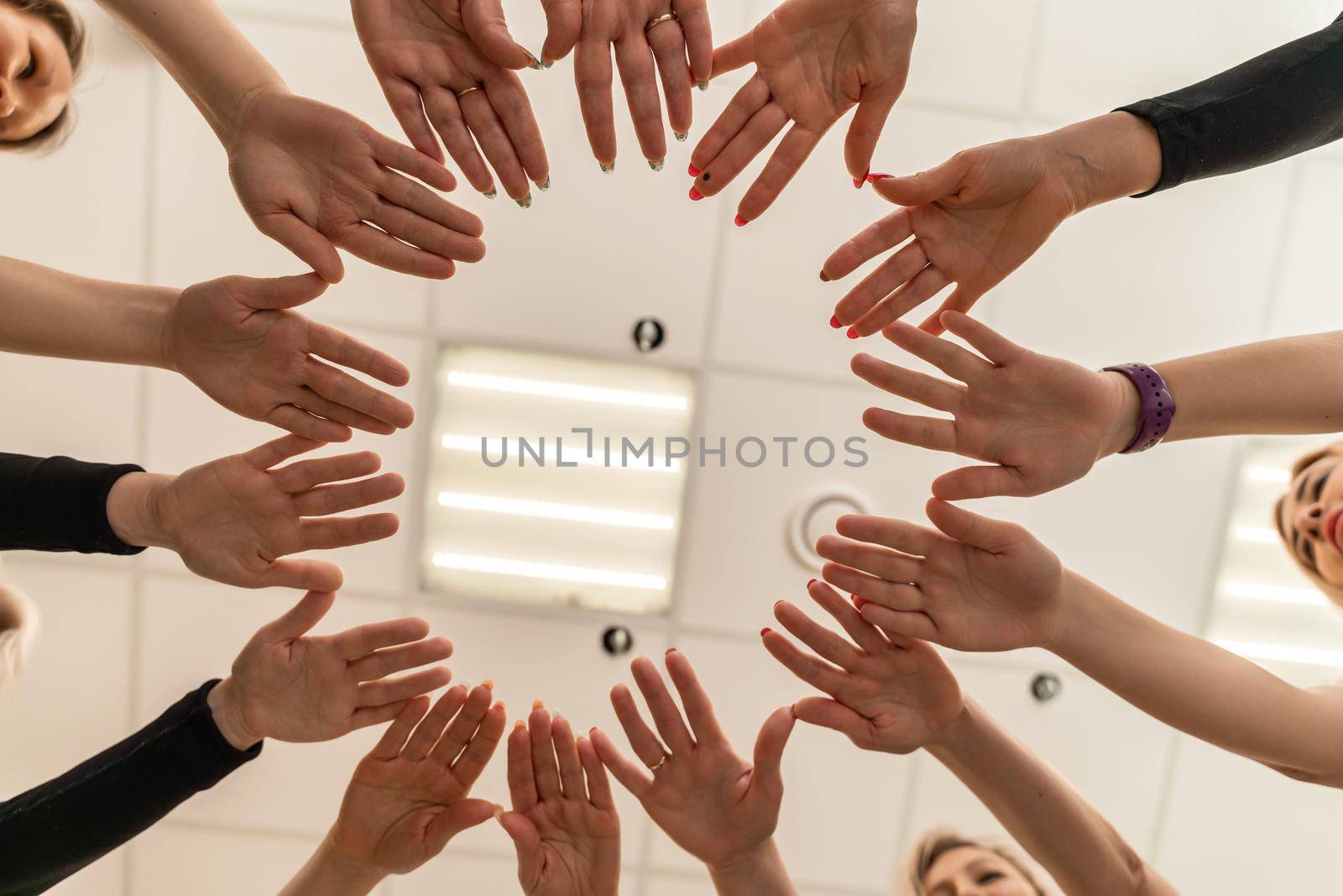 Team of people holding hands. Group of happy young women holding hands. Bottom view, low angle shot of human hands. Friendship and unity concept by Matiunina