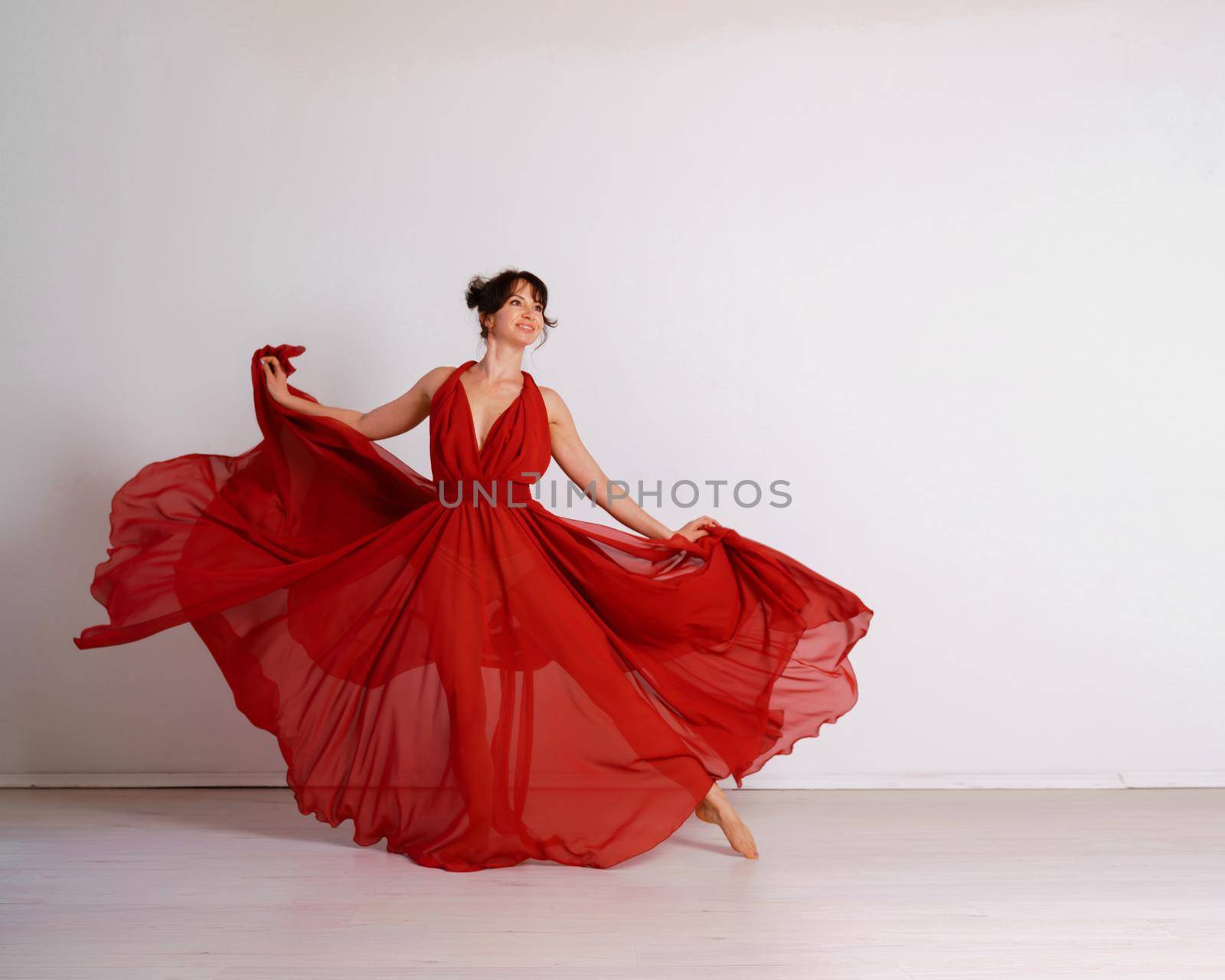 Dancer in a red flying dress. Woman ballerina dancing on a white studio background.