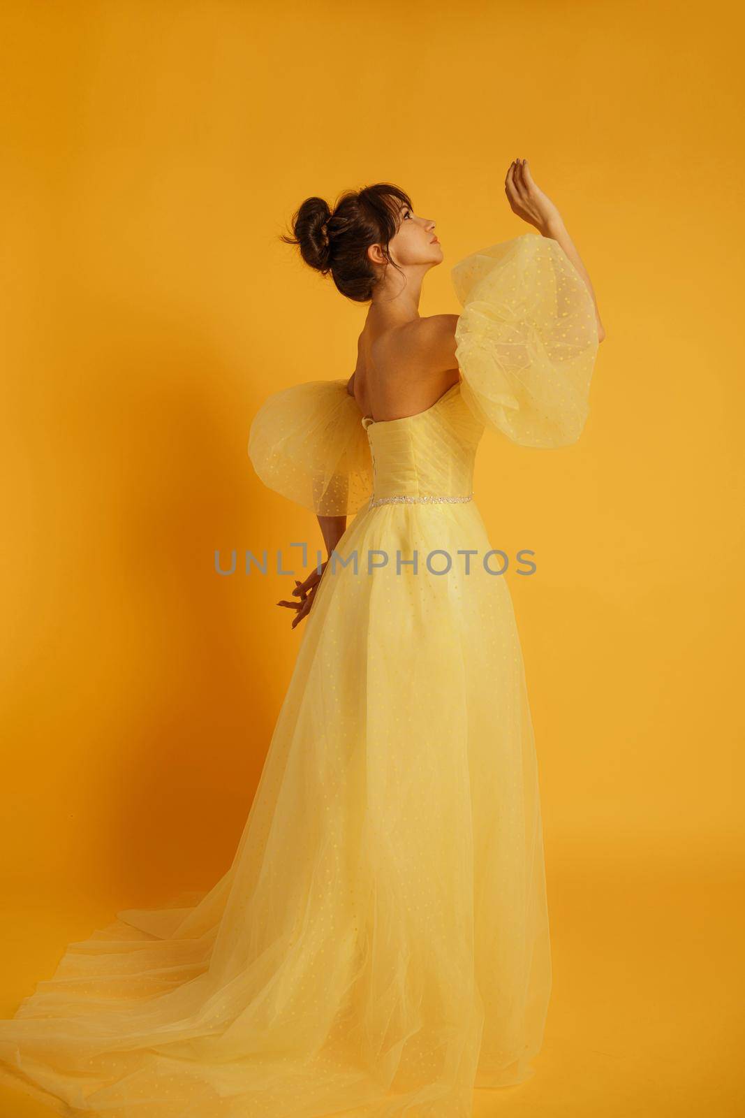 Profile portrait of a beautiful middle-aged woman in a yellow dress, her hair pulled up against a yellow background.