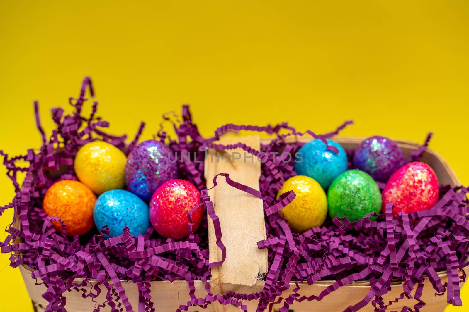 Easter composition from a basket and colored eggs prepared for the holiday on a yellow background.