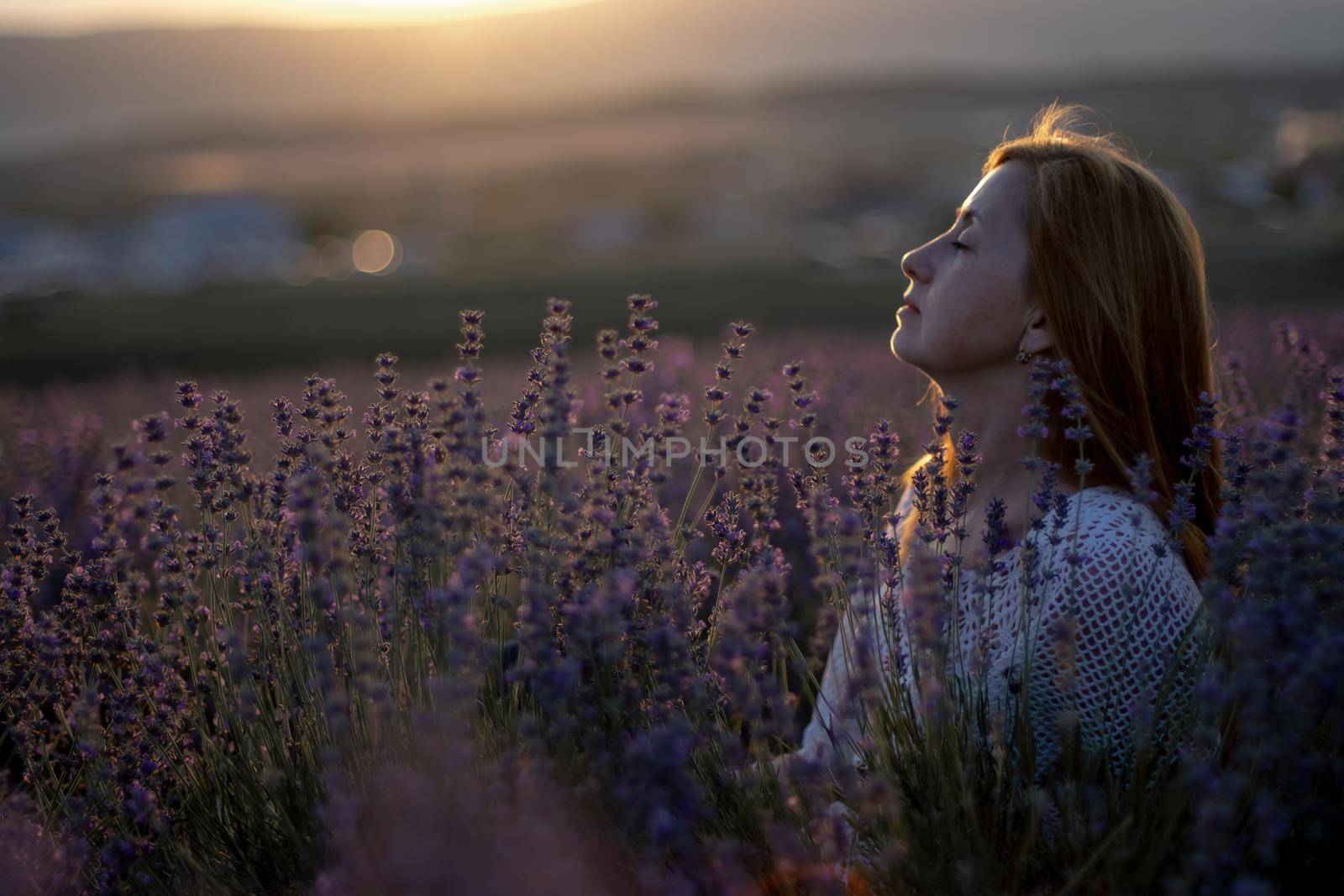 A middle-aged woman sits in a lavender field and enjoys aromatherapy. Aromatherapy concept, lavender oil, photo session in lavender by Matiunina