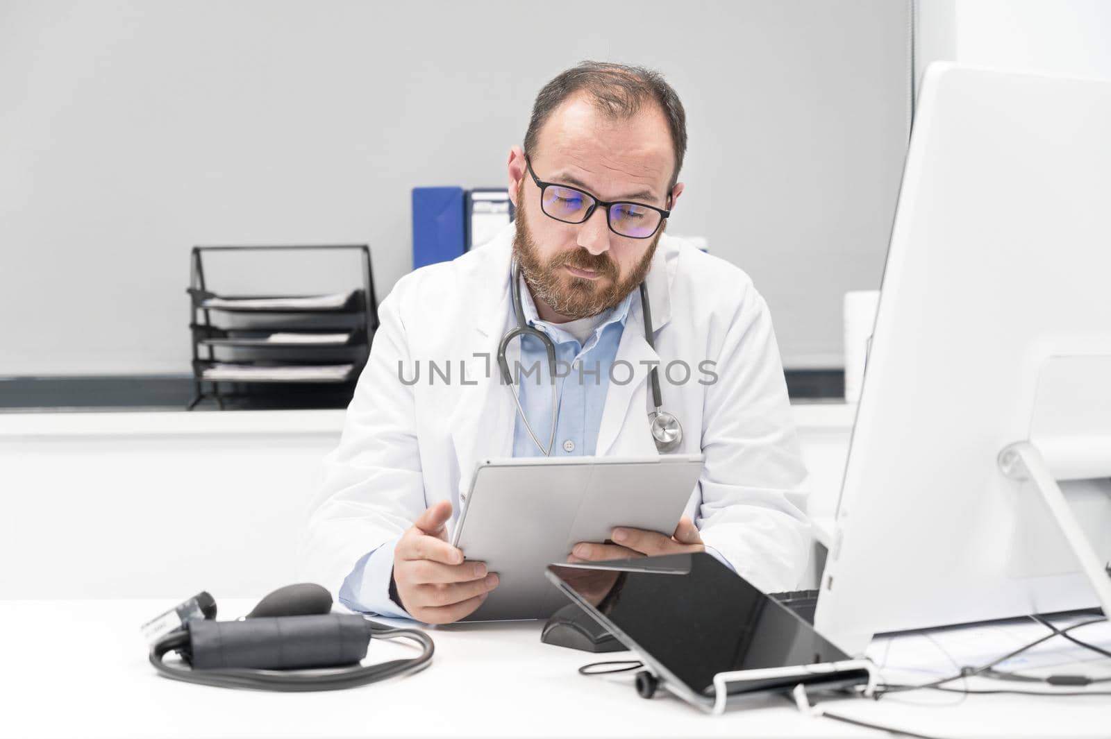 Doctor using his tablet computer at work by HERRAEZ