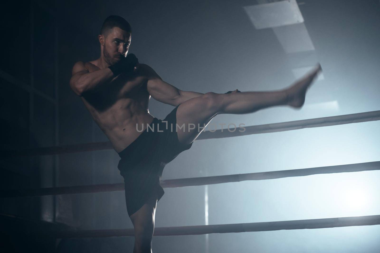 Muscular MMA fighter practicing kick, fight club concept. by HERRAEZ