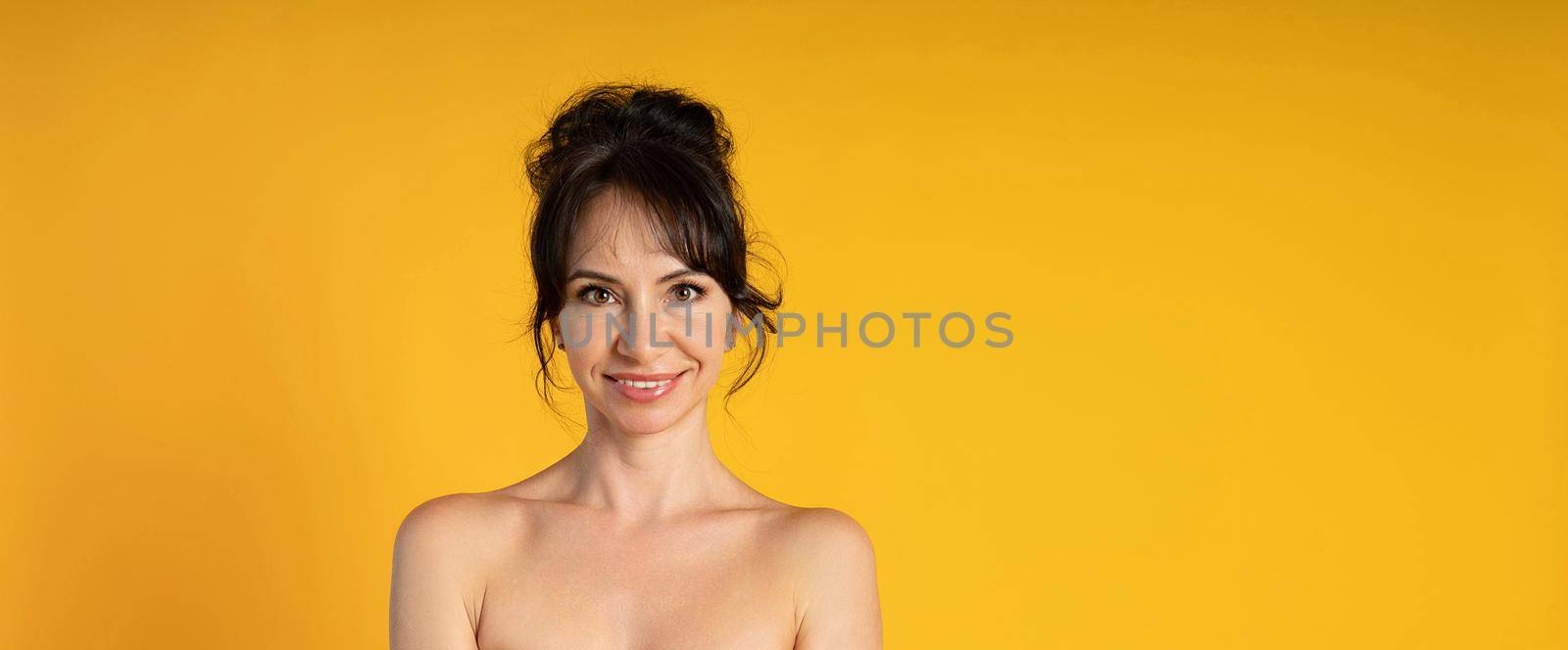 Smiling beautiful middle-aged woman on a yellow background in the studio. by Matiunina