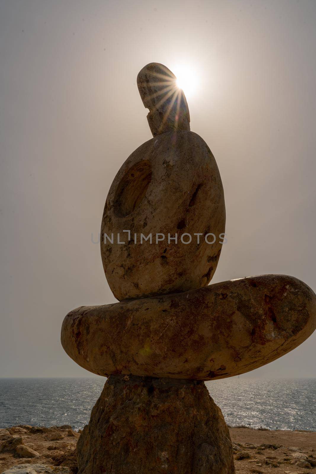 Sculpture symbol made of large pebbles against the blue sky by Matiunina