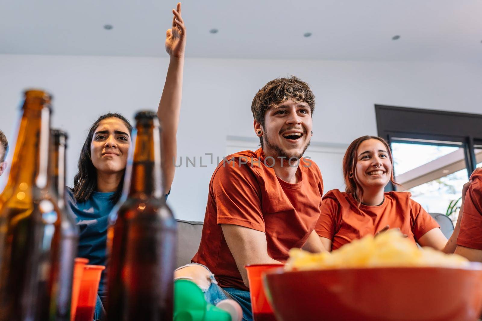 friends hugging after the victory of their sports team broadcast on television. group of young people partying at home. concept leisure concept. happy and cheerful. natural light in the living room at home. trumpet