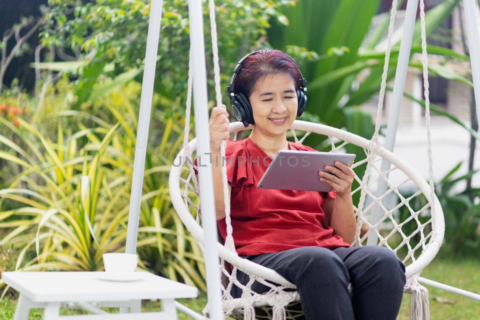 Middle aged woman relaxing on swing listen music on the tablet computer in backyard..