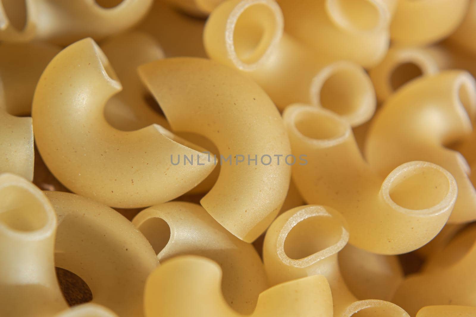 Macaroni raw background. Curved hollow horns for making macaroni cheese. Backdrop for a culinary theme. Selective focus.