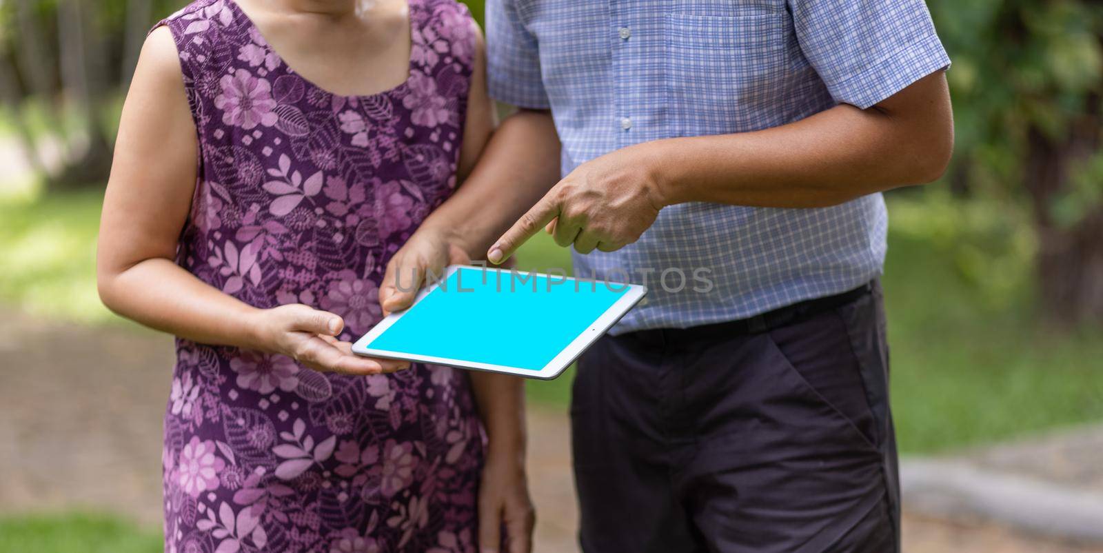 Asian middle-aged couple talking and look at tablet together in backyard.