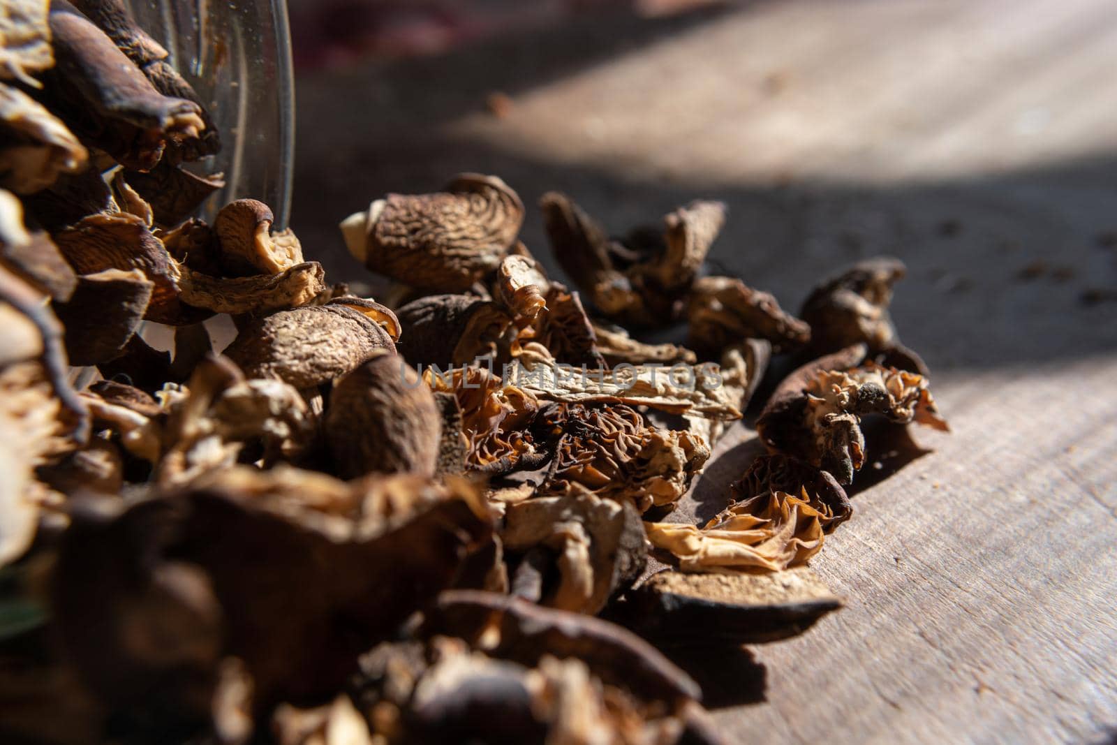 Dried mushrooms scattered from a glass jar on a wooden table illuminated by the sun. Selective focus. Culinary theme.
