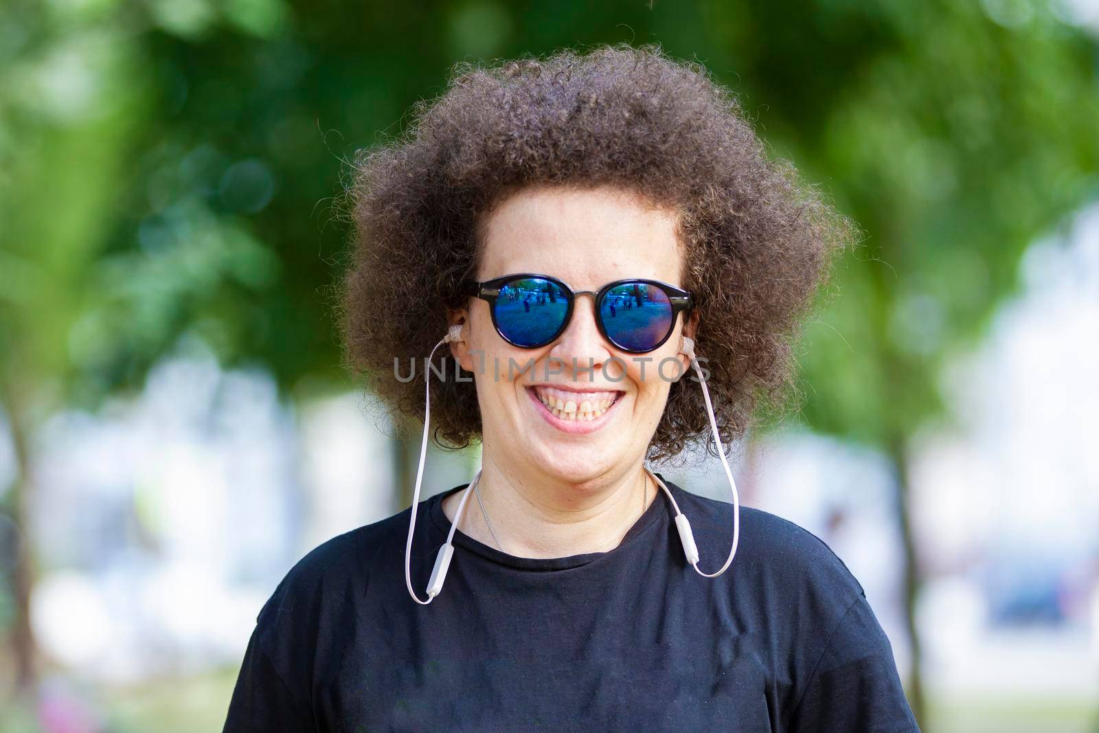 Curly girl in sunglasses looks at the camera and smiles.