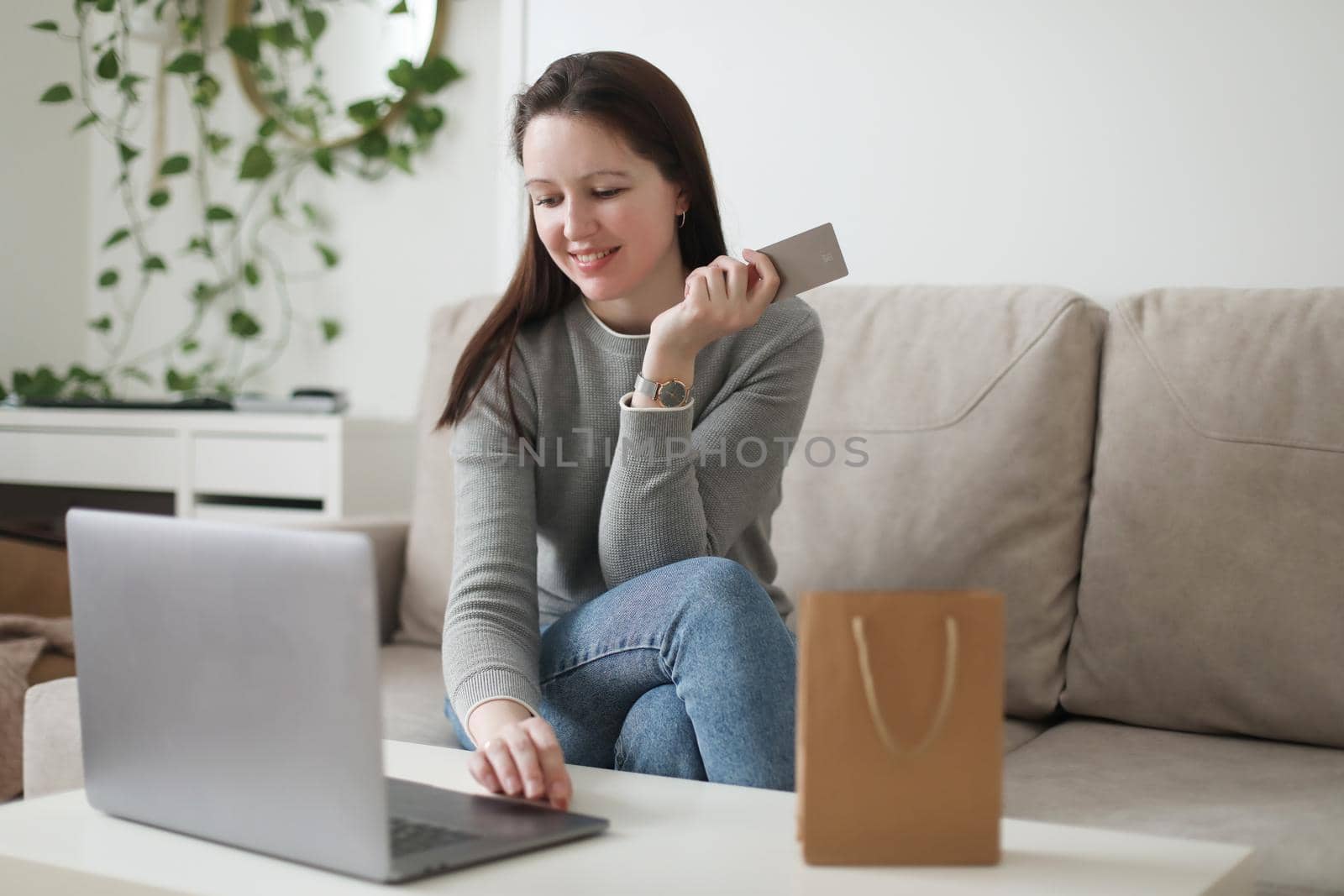 Young woman holding credit card and using laptop at home. Paying online, home shopping, internet banking, electronic store concept.