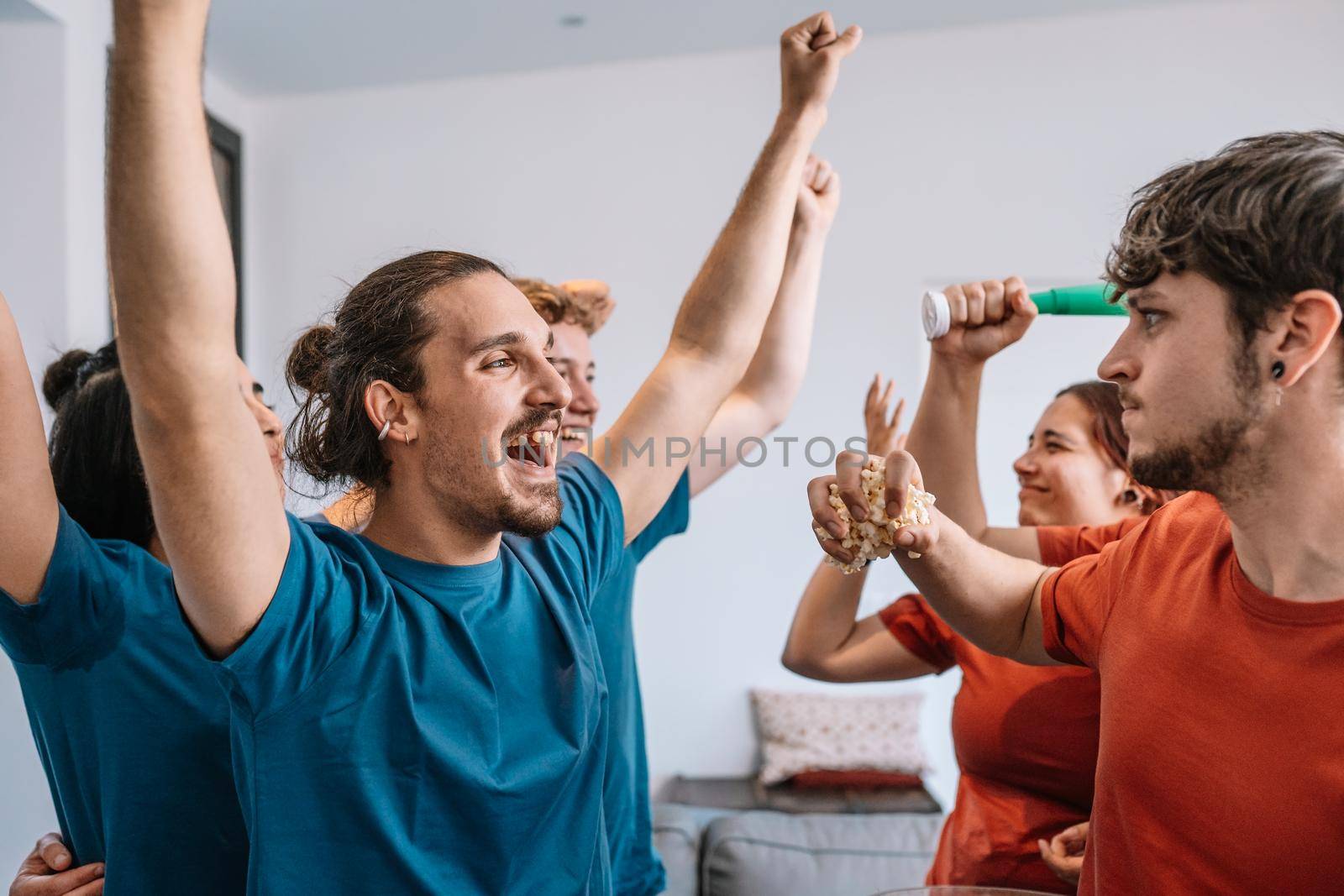 group of friends watching a sports championship on TV losing team throws popcorn at the winning team. leisure concept. happy and cheerful. natural light in the living room at home. trumpet