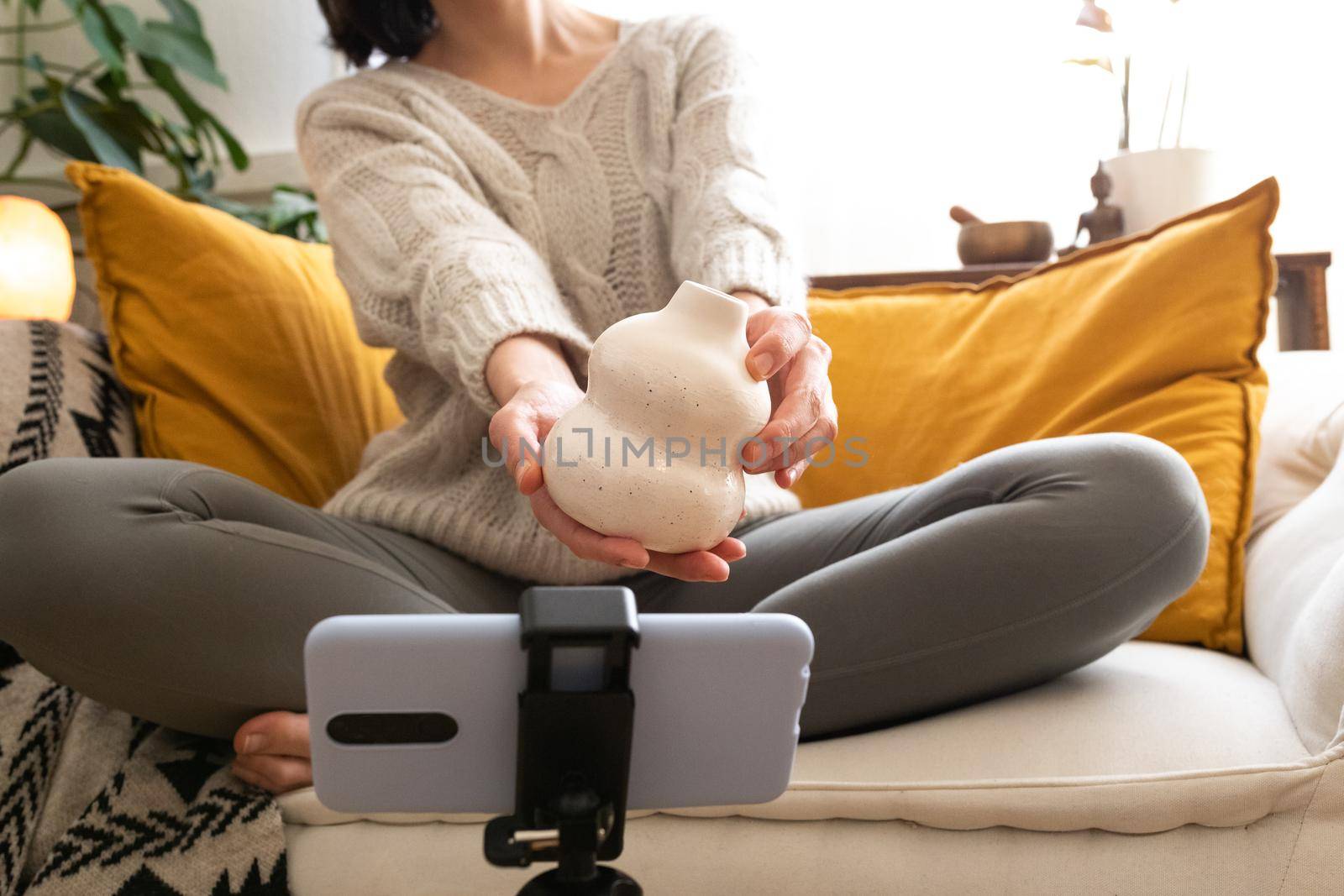 Unrecognizable young woman showing handmade artisan ceramic vase during video call with mobile phone. Technology concept