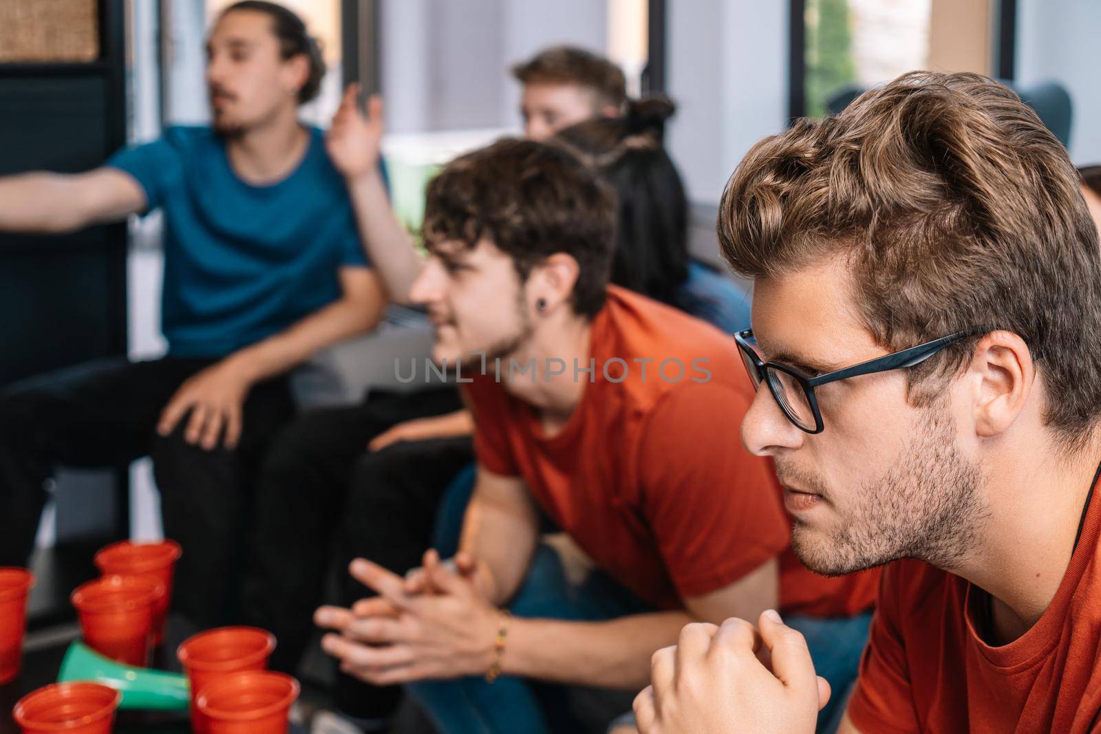 friends concentrating on watching e-sports on TV after their team's victory. group of young people partying at home. leisure concept. happy and cheerful. natural light in the living room at home. trumpet