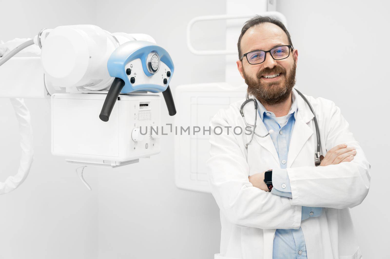 Smiling confident radiologist standing near x-ray equipment.. by HERRAEZ