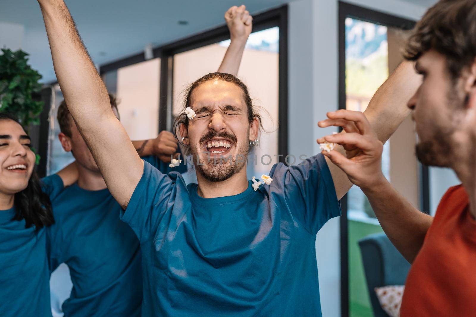 group of friends jumping for joy after the victory of their soccer team. losing team throws popcorn at the winning team. leisure concept. happy and cheerful. natural light in the living room at home. trumpet