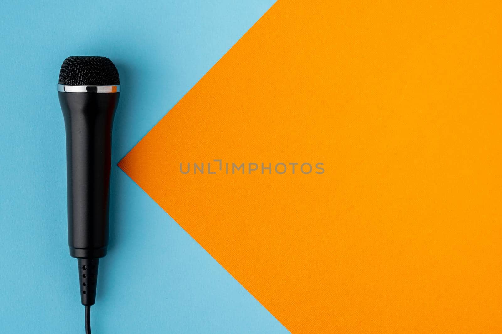 Cable black microphone on colorful blue and orange background, directly above, copy space. Musical professional studio equipment. Modern broadcasting concept. Karaoke entertainment mockup