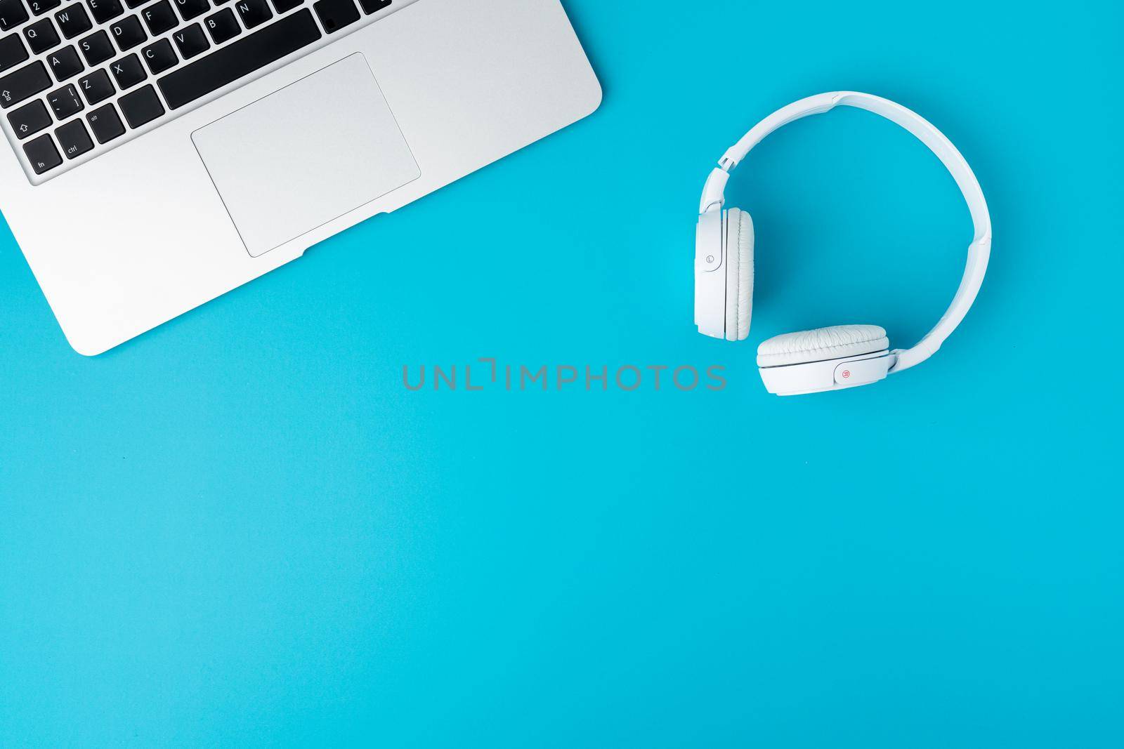 Horizontal flat lay of white digital tech headphones and cropped keyboard laptop on turquoise background, copy space. Concept of broadcasting, audio listening device