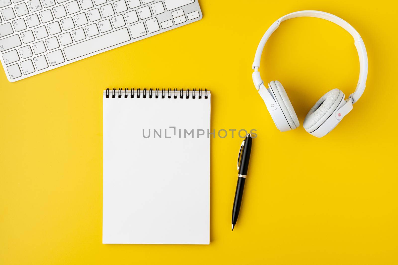 Blank notepad with fountain pen, portable keyboard and headphones on bright yellow background. Workspace office surface. Wireless technology concept, copy space, horizontal, overhead